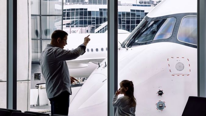 Otac i dete na aerodromu posmatraju avion kroz staklo terminala